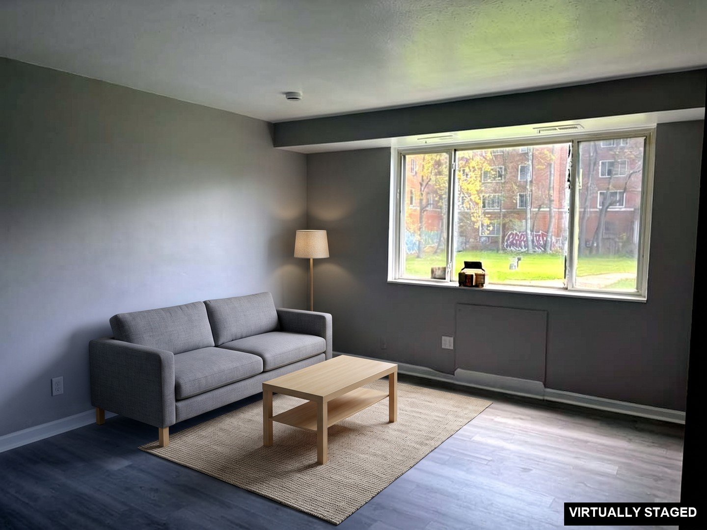 1 Bedroom Apartment at Superior Hill #7B, East Cleveland OH — Empty living room with gray walls, wood-look flooring and a large window. (virtually staged)