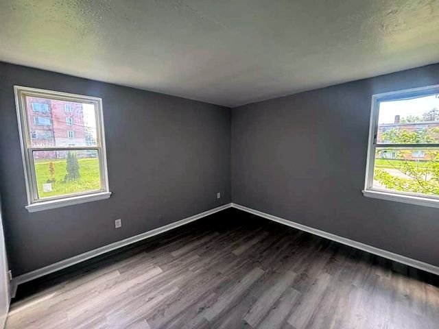 1 Bedroom Apartment at Superior Hill #7B, East Cleveland OH — Empty living room with gray walls, wood-look flooring, and two windows.