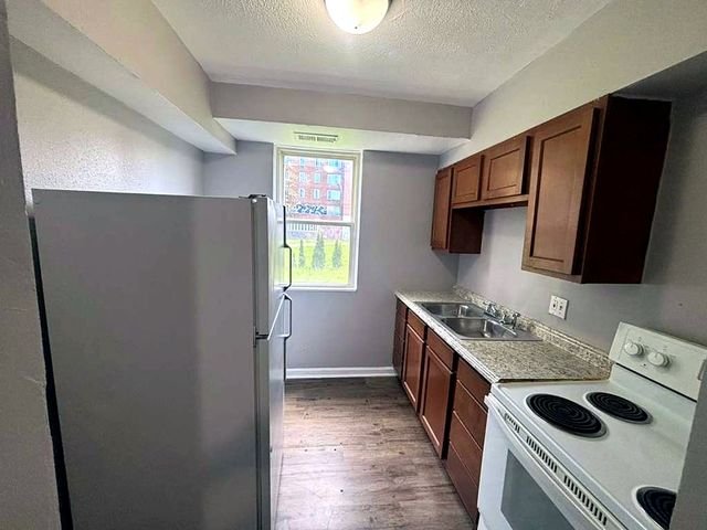 1 Bedroom Apartment at Superior Hill #7B, East Cleveland OH — A kitchen with brown cabinets, stainless steel appliances and linoleum flooring.