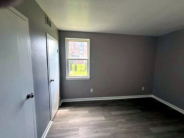 1 Bedroom Apartment at Superior Hill #7B, East Cleveland OH — Bedroom with gray walls, wood-look flooring, and a window showing an exterior view.