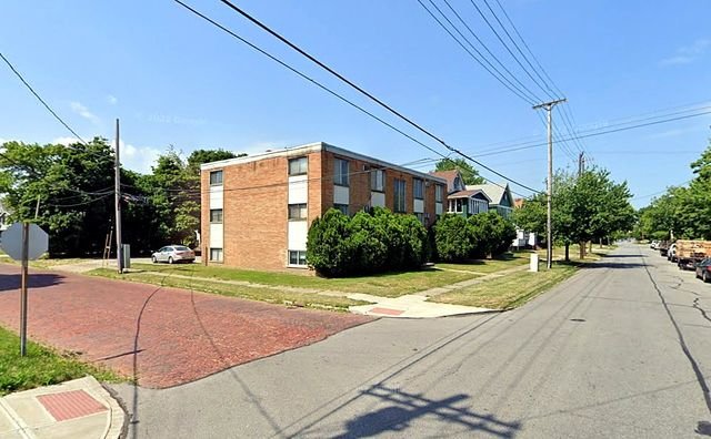 1 Bedroom Apartment at Grovewood #2, Cleveland OH — A brick apartment building sits on the corner of a street with trees and utility poles.