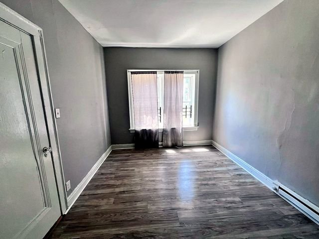 1 Bedroom Apartment at Linn #9, Cleveland OH — A room with gray walls, wood-look flooring, and a window covered by sheer curtains.
