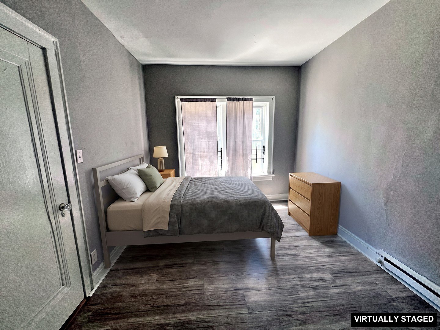 1 Bedroom Apartment at Linn #9, Cleveland OH — A room with gray walls, wood-look flooring, and a window covered by sheer curtains. (virtually staged)