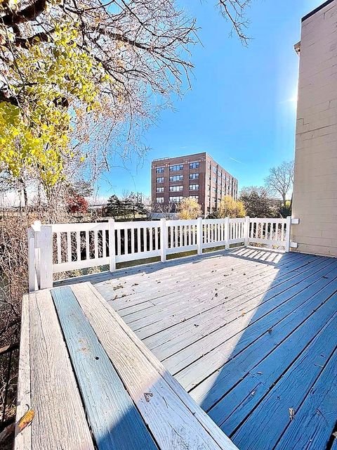 Studio Apartment at Lux Apartments #136, Toledo OH — A deck with blue-painted wood flooring and white railings overlooks trees and a building.